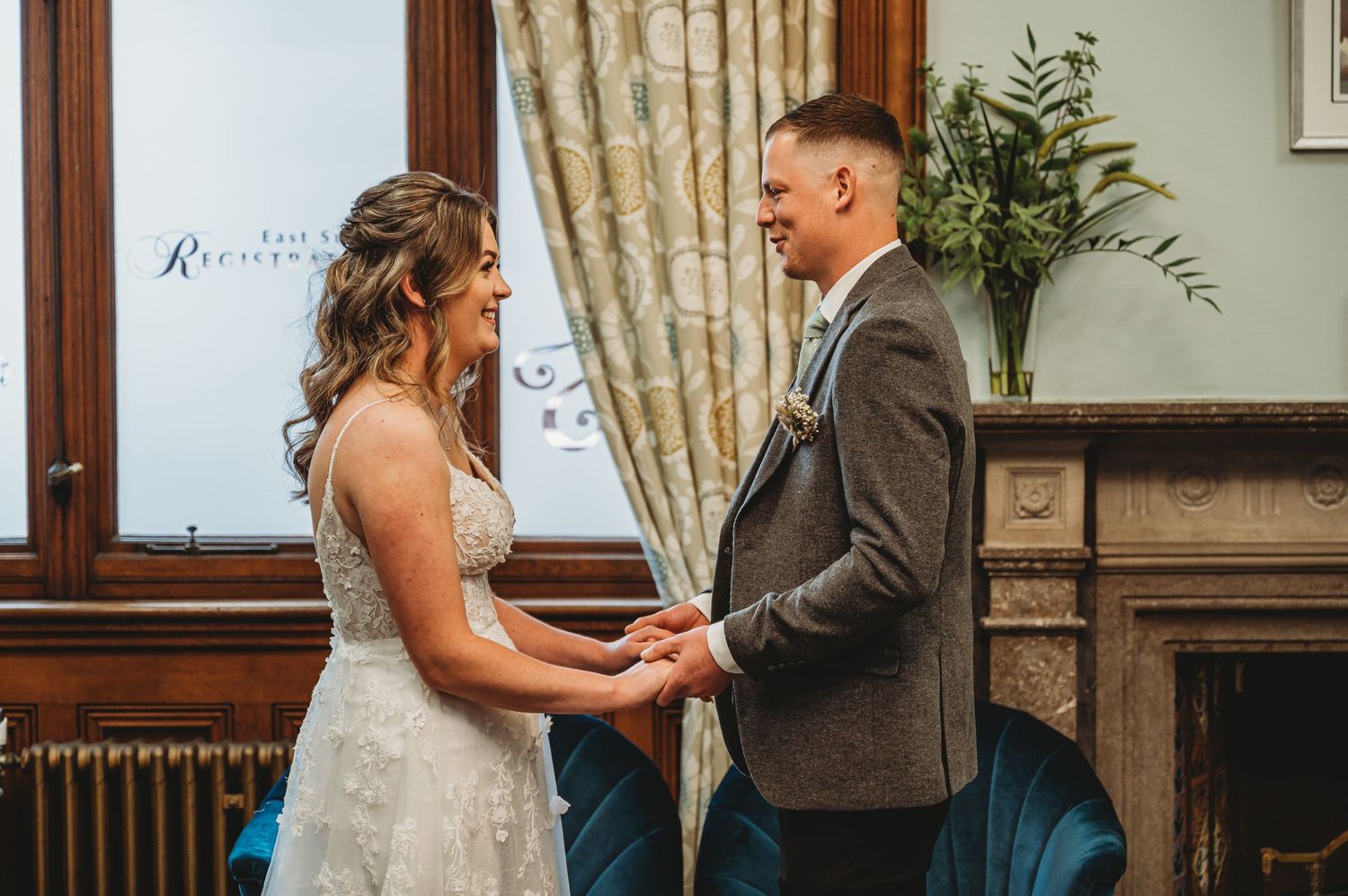 A couple shares an intimate moment during their wedding ceremony in front of a window and vintage fireplace.