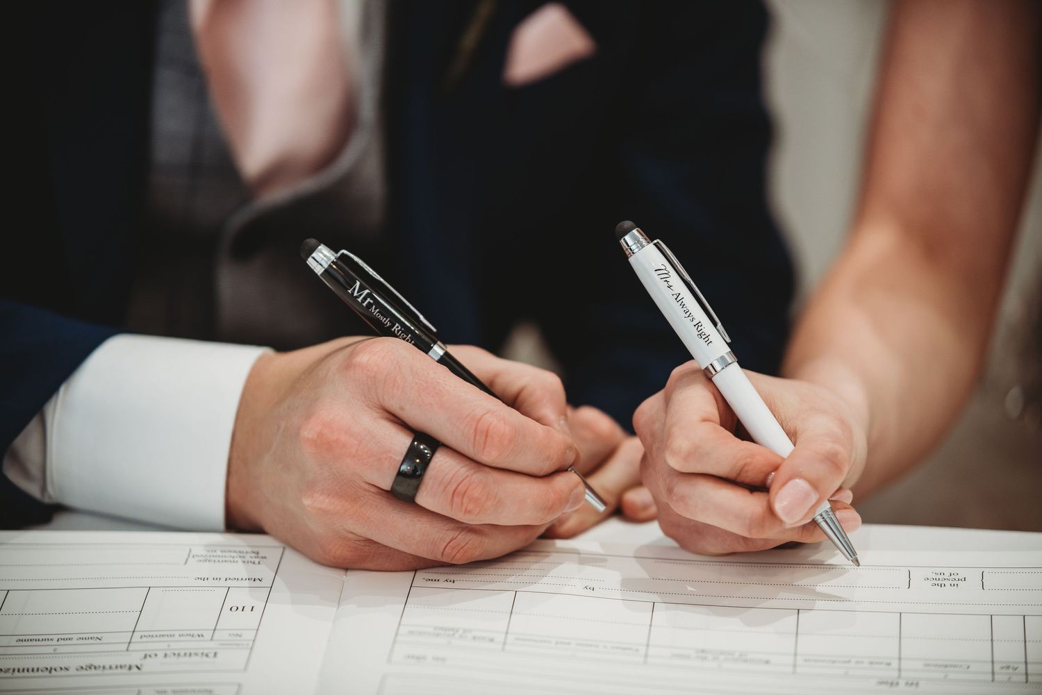 Close-up view of two hands signing official documents with pens on white paperwork.