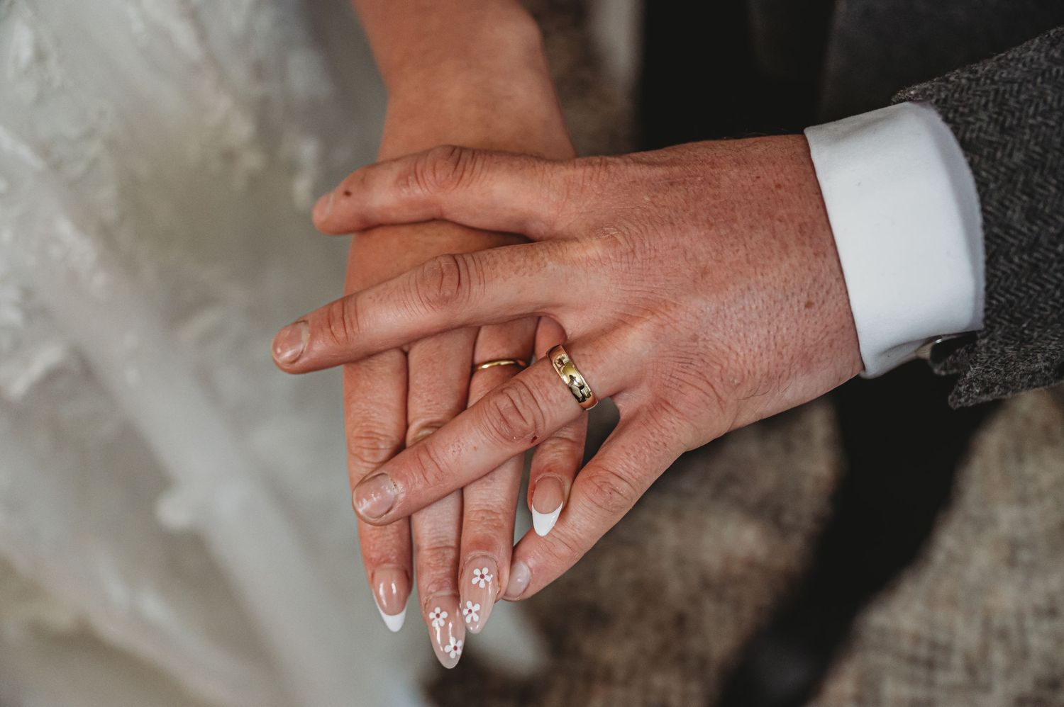 Two hands with wedding rings gently touch during a romantic wedding moment.