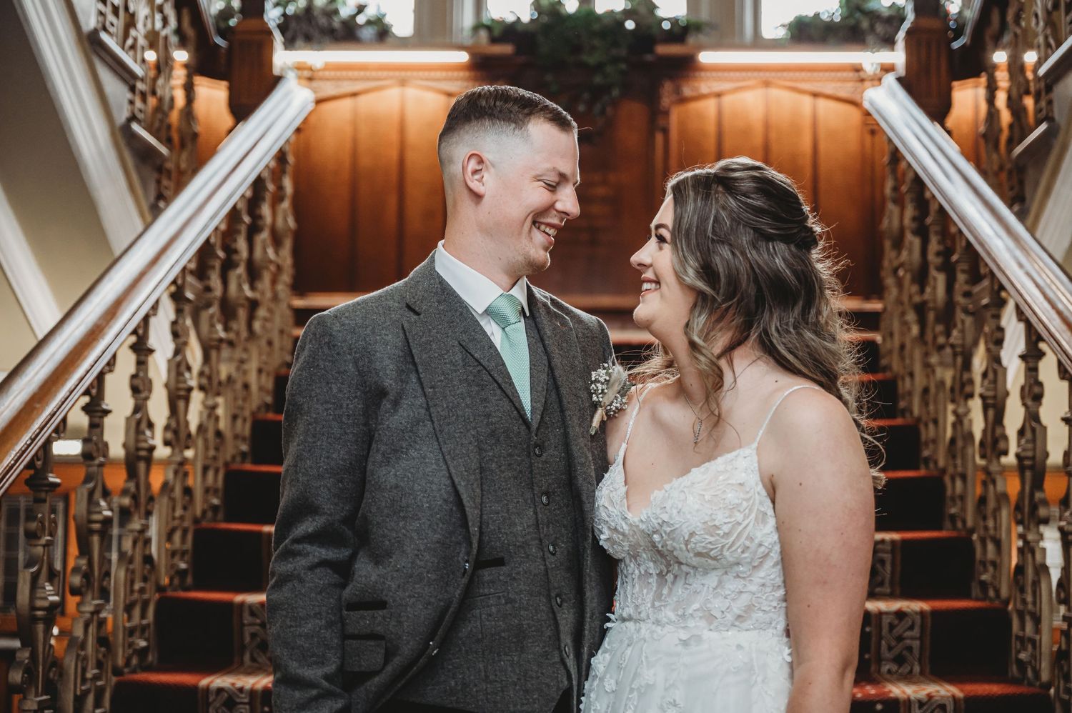 A couple shares a loving moment together on an elegant wooden staircase during their wedding celebration.