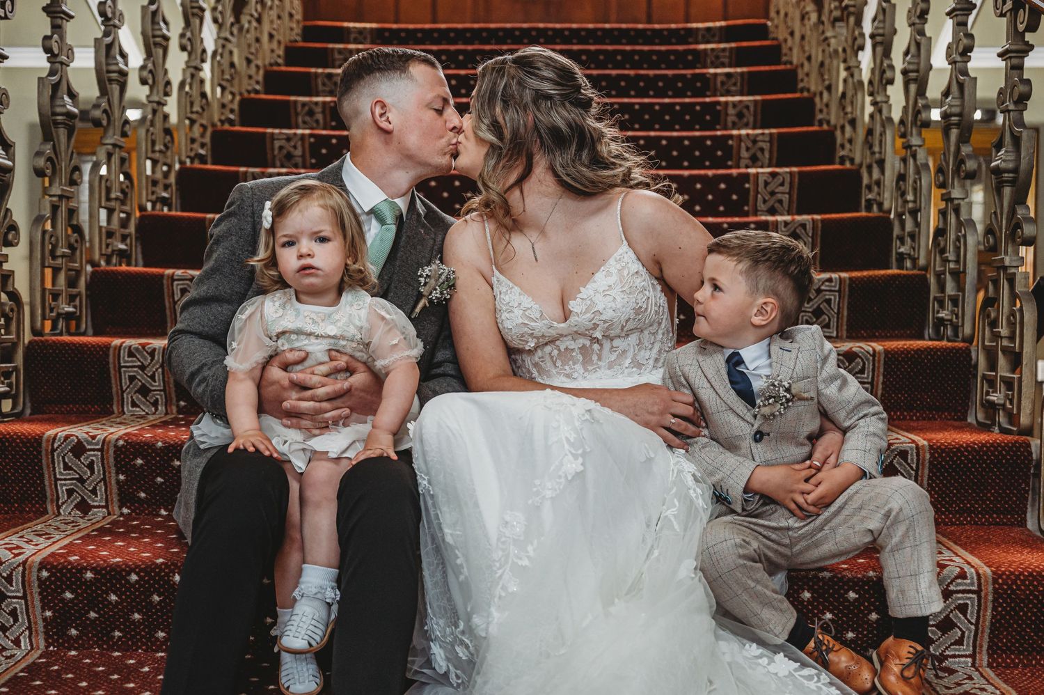 Intimate family portrait captured on elegant carpeted stairs with ornate gold railings and chandelier lighting.