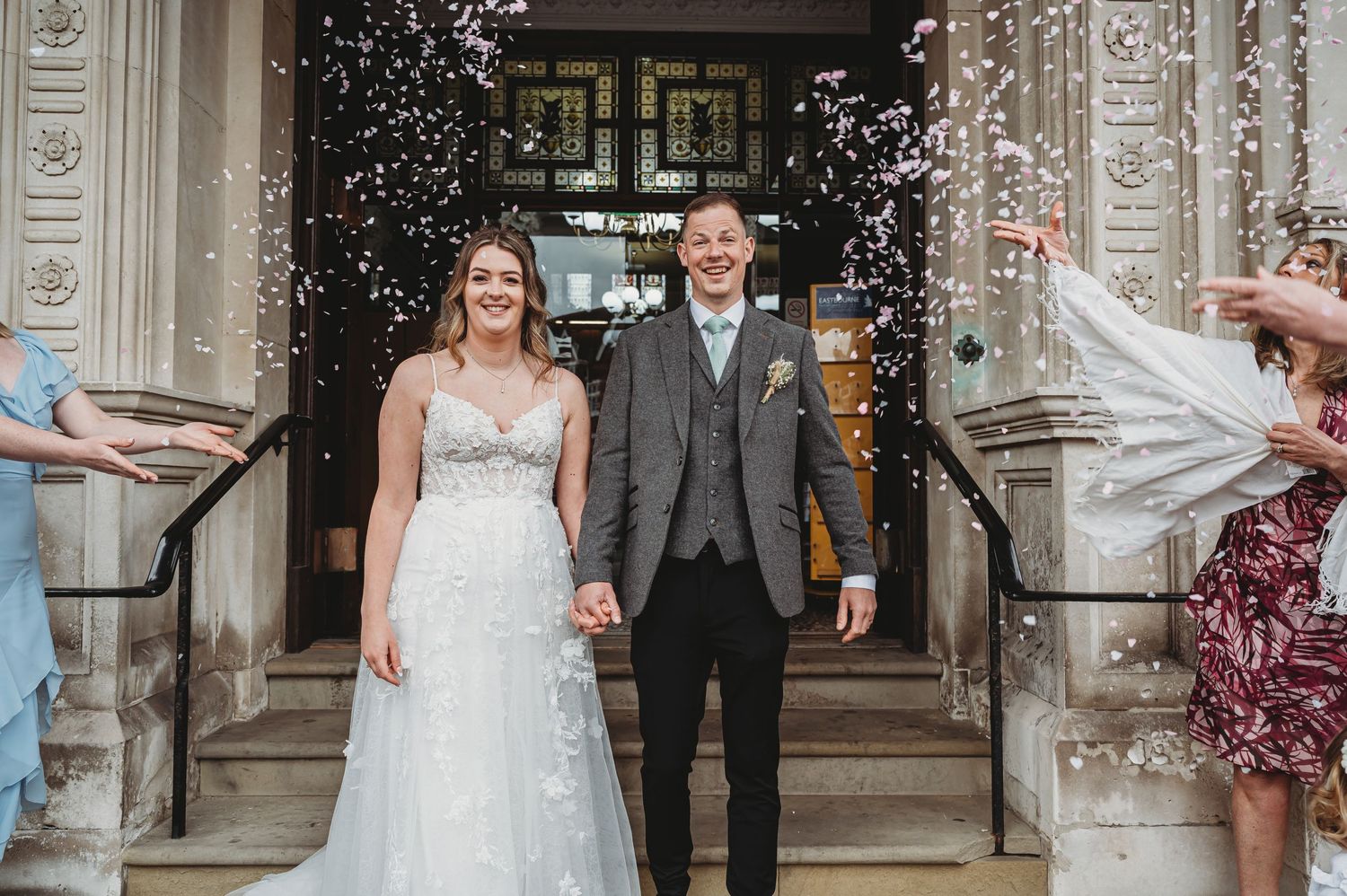 Wedding couple exits ceremony as wedding guests shower them with confetti on grand stone steps.