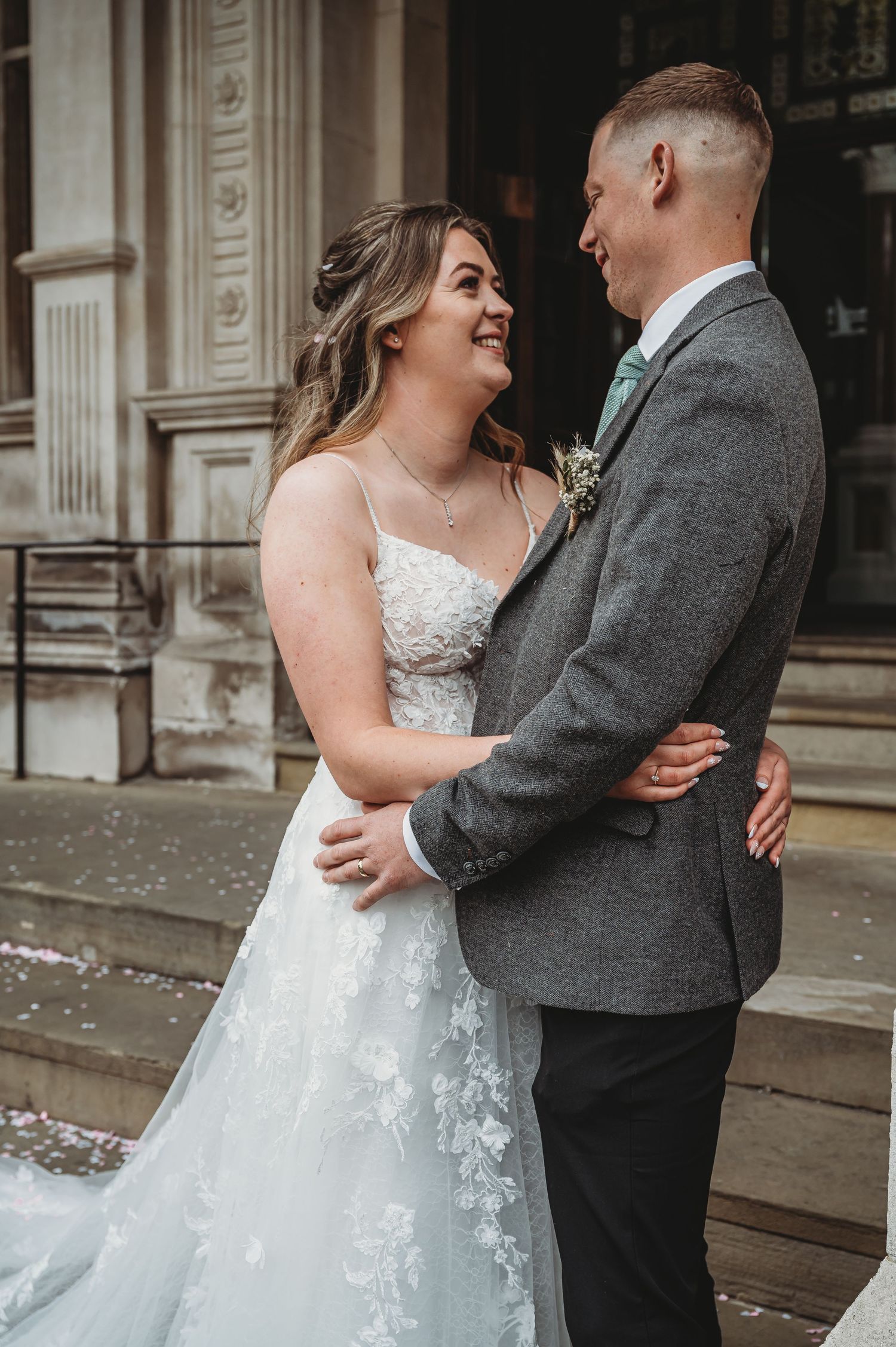 A couple shares a joyful moment together at their wedding, the bride in a lace gown and groom in a gray suit.