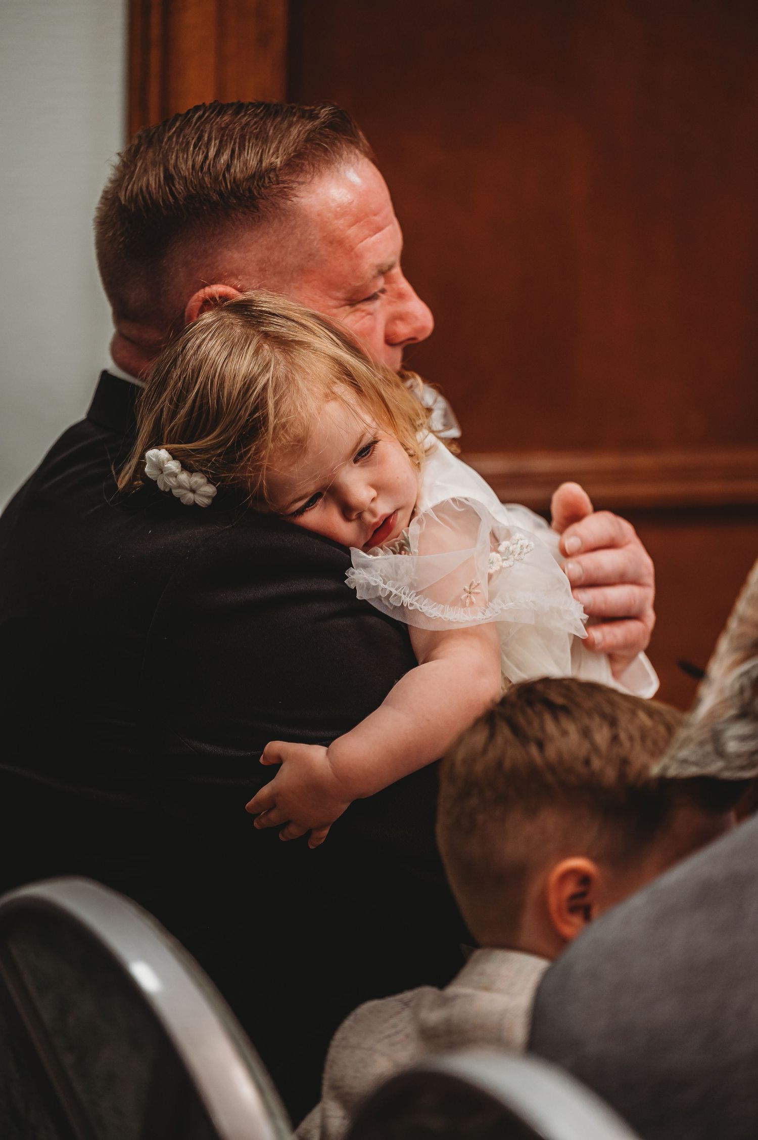 A touching emotional moment at a wedding as a small child in white lace hugs an adult in formal attire.