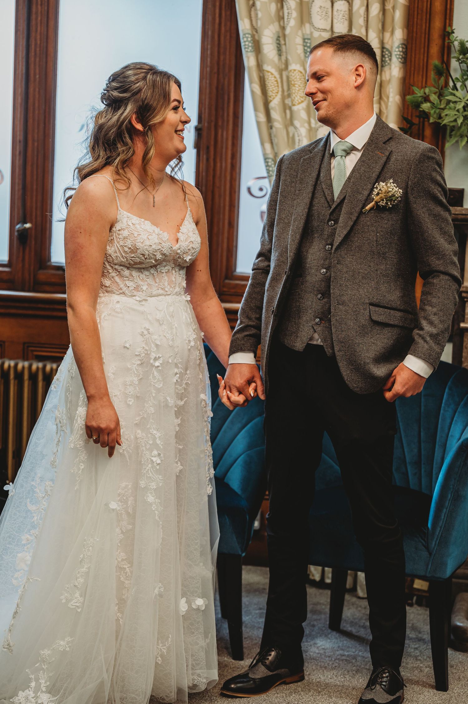 A bride in a beaded white gown and groom in a brown suit share a joyful moment during their wedding ceremony.