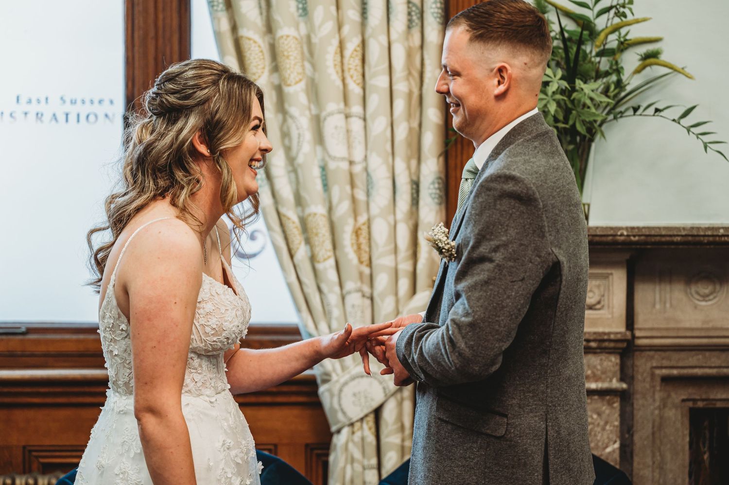 Two people share an intimate moment during their wedding ceremony in a room with elegant curtains and decor.