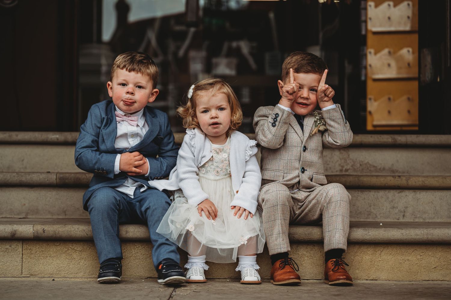 Three young children sit together on stone steps wearing casual clothing in a candid outdoor portrait.