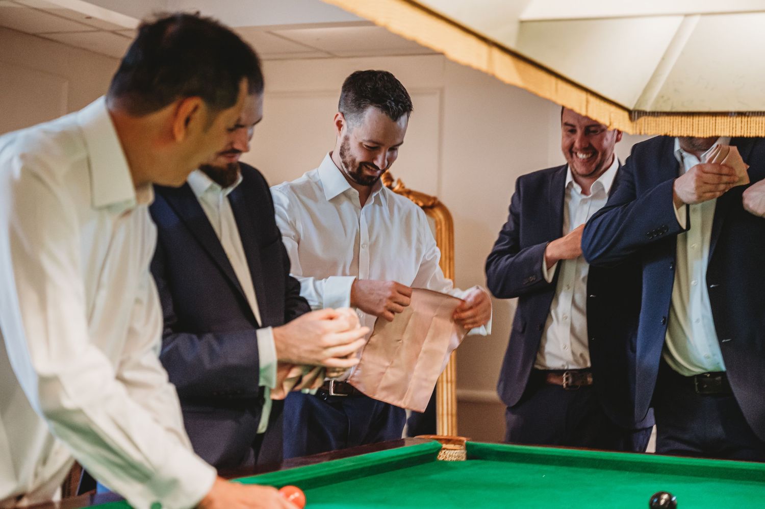 A group of formally dressed people gather around a pool table during a social event under a tent canopy.