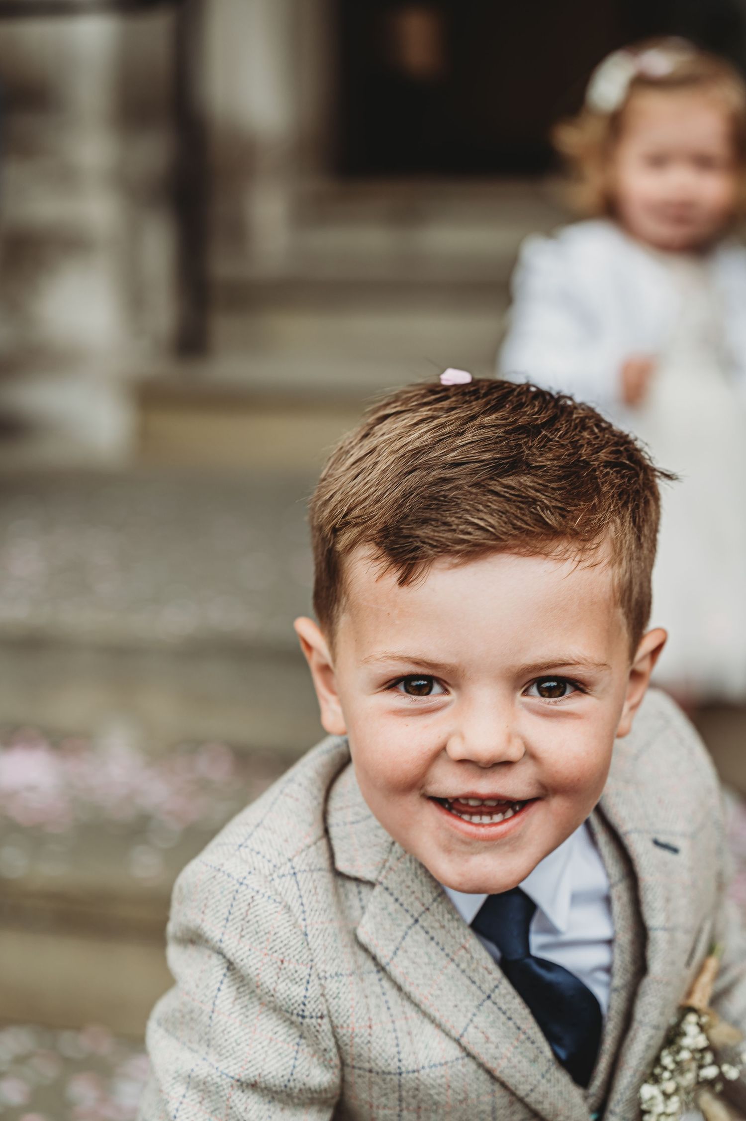 A child wearing a light gray suit jacket and blue tie smiles warmly at the camera during what appears to be a formal event.