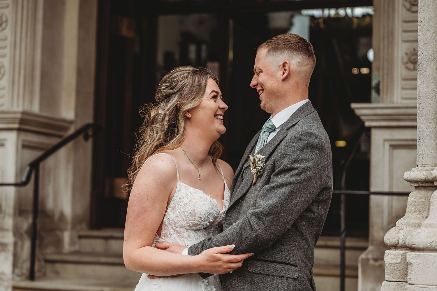 A joyful couple sharing a candid laughing moment together on their wedding day outside a historic building.