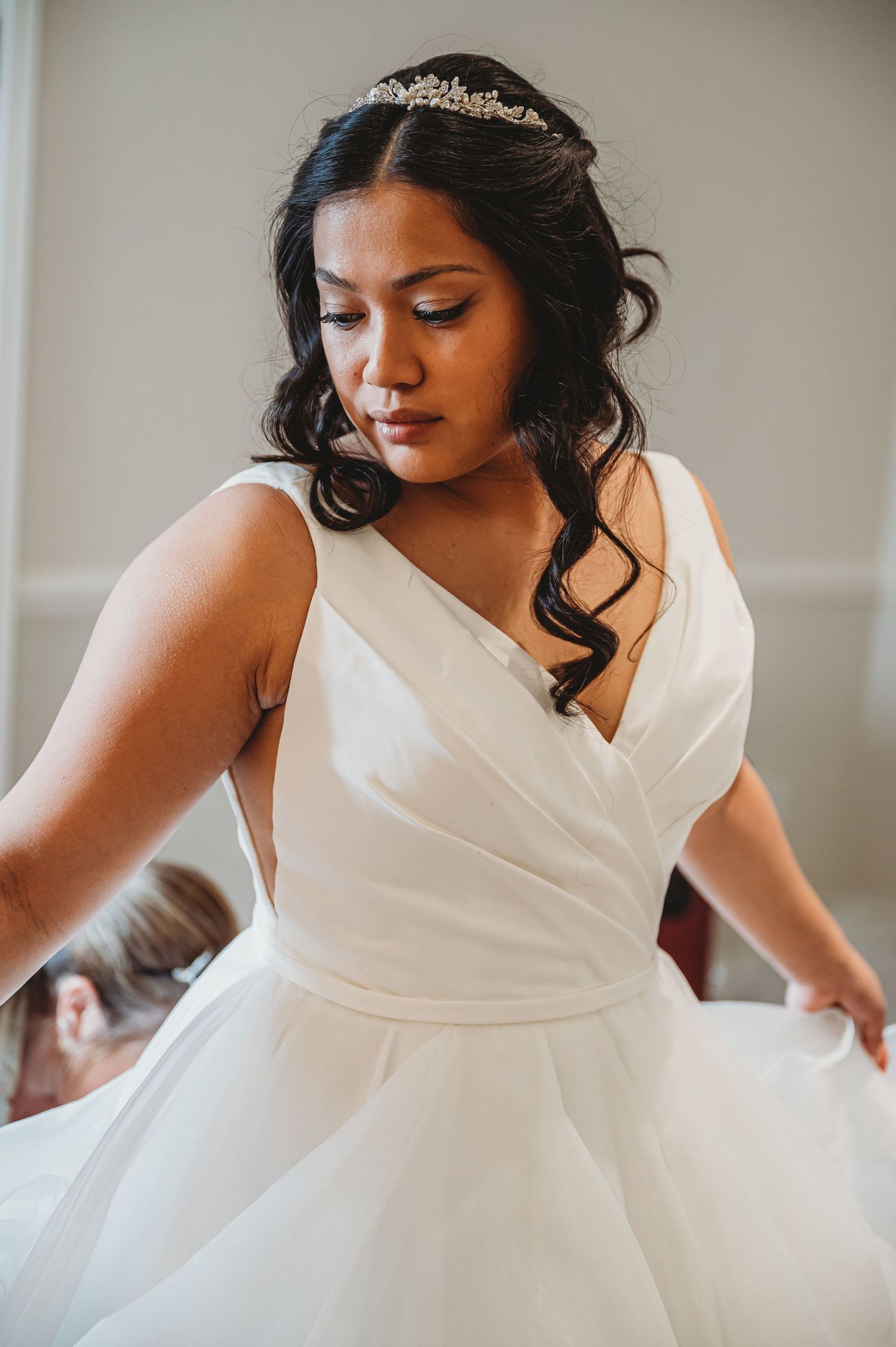 An elegant bride in a white wrap-style ballgown with tiara and cascading curls twirls during her wedding day.
