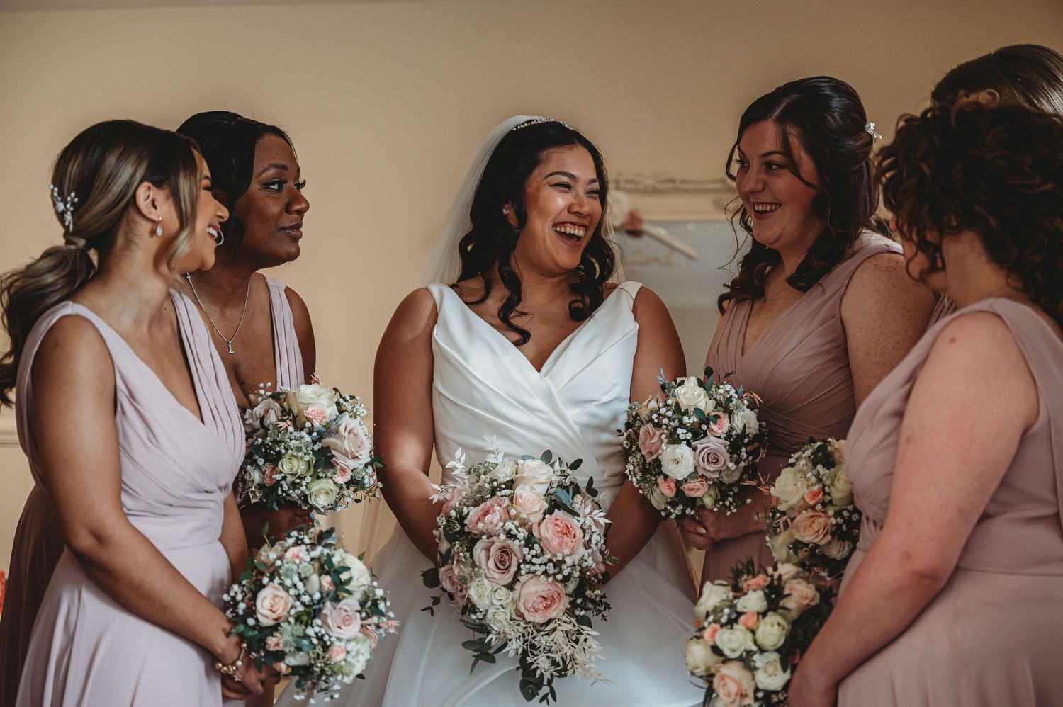 A bridal party shares a joyful moment together while holding pink and white floral bouquets.