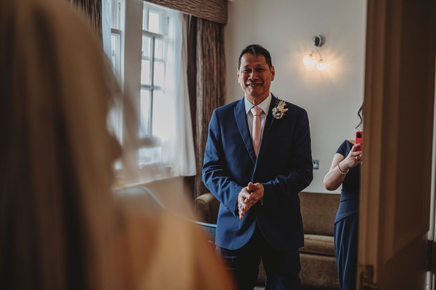 Joyful person wearing a blue suit and tie stands near a window at a formal event.