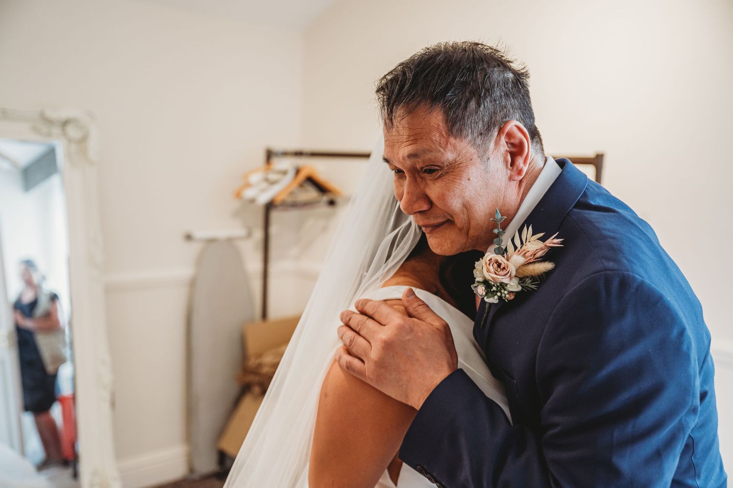 An emotional moment captured during a wedding as someone in a navy suit embraces another person while wearing a boutonniere.