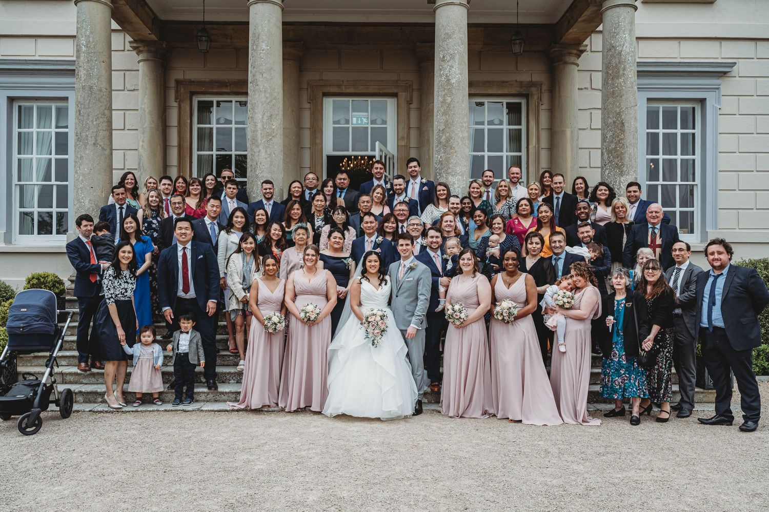 Large wedding party poses on grand stone steps outside historic building with columns.