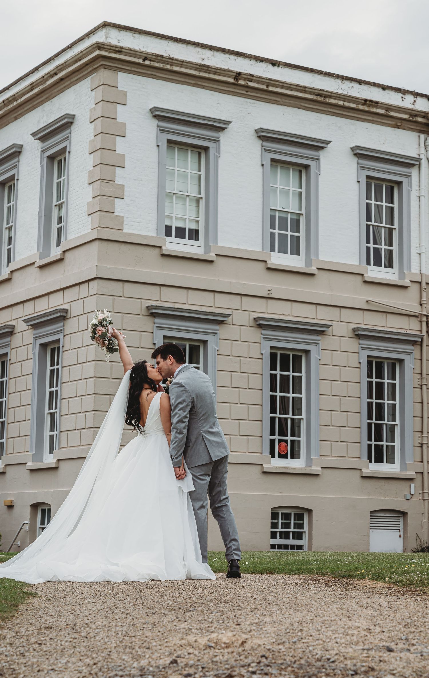 Elegant wedding couple embraces outside a historic Georgian style building with white windows and stone facade.