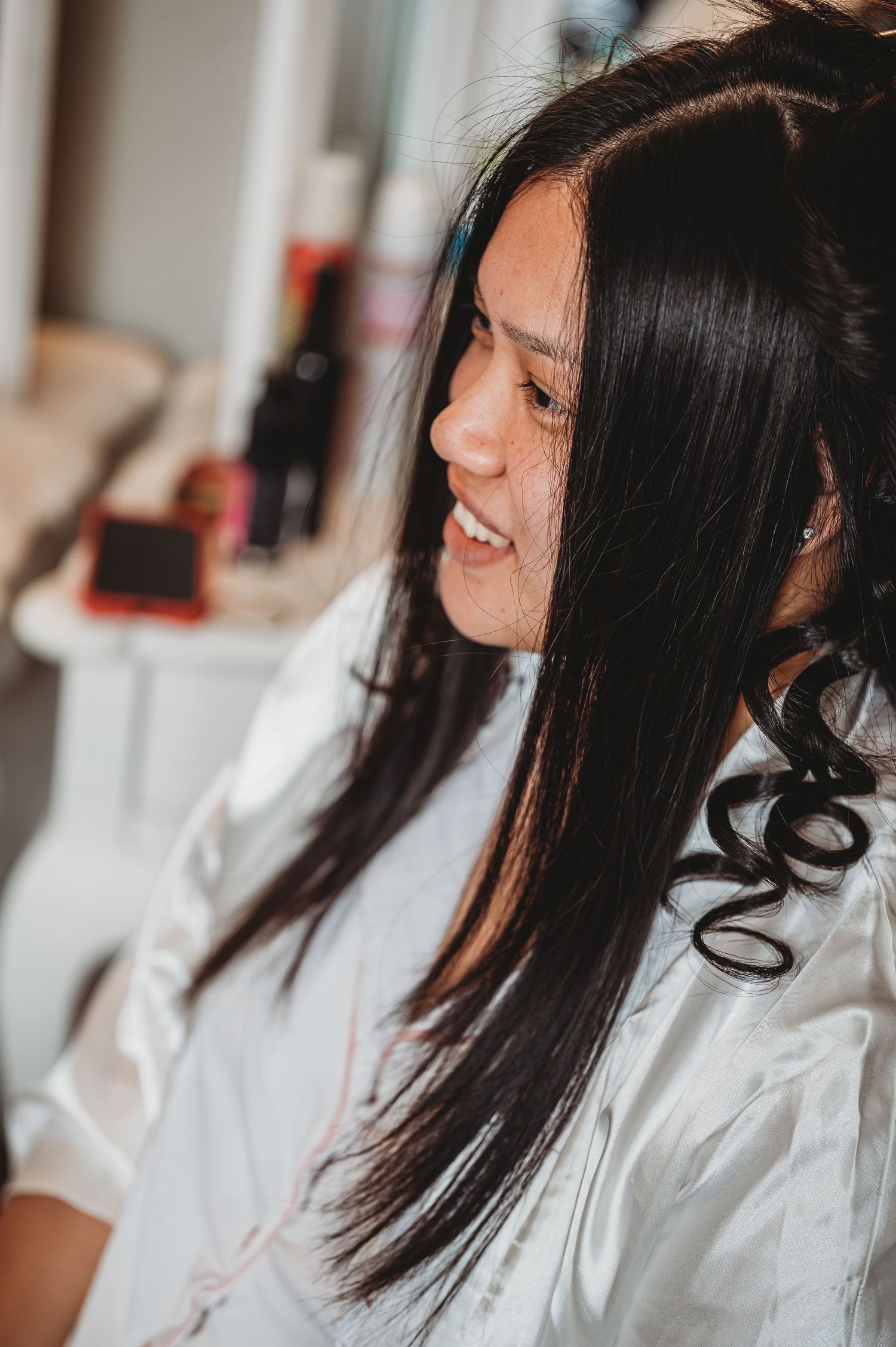 Woman with long dark straight hair wearing a white silk robe getting ready for a special occasion.