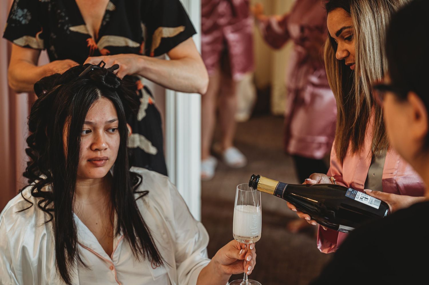 Someone gets their hair styled while enjoying champagne as stylists work in a warm-toned salon setting.