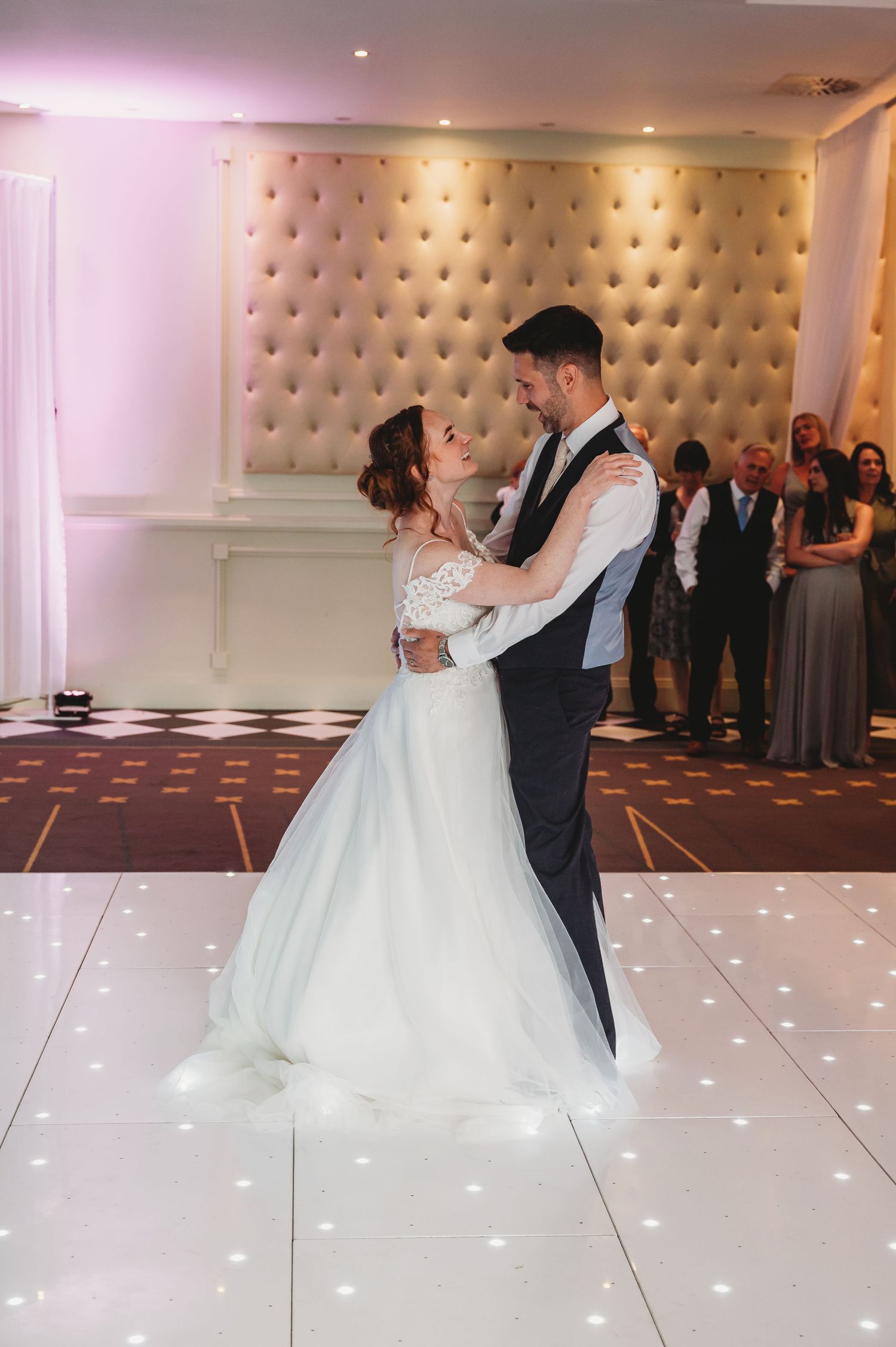 A couple shares their first dance on an illuminated dance floor during their wedding reception.