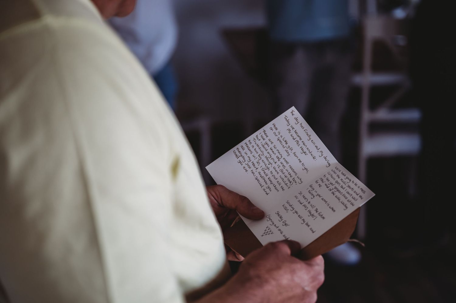 Someone in a white sweater holds and reads a small paper slip or receipt in a dimly lit setting.