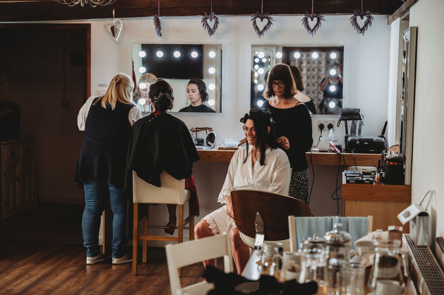 Beauty salon interior with clients getting hair styled at makeup stations with illuminated mirrors.