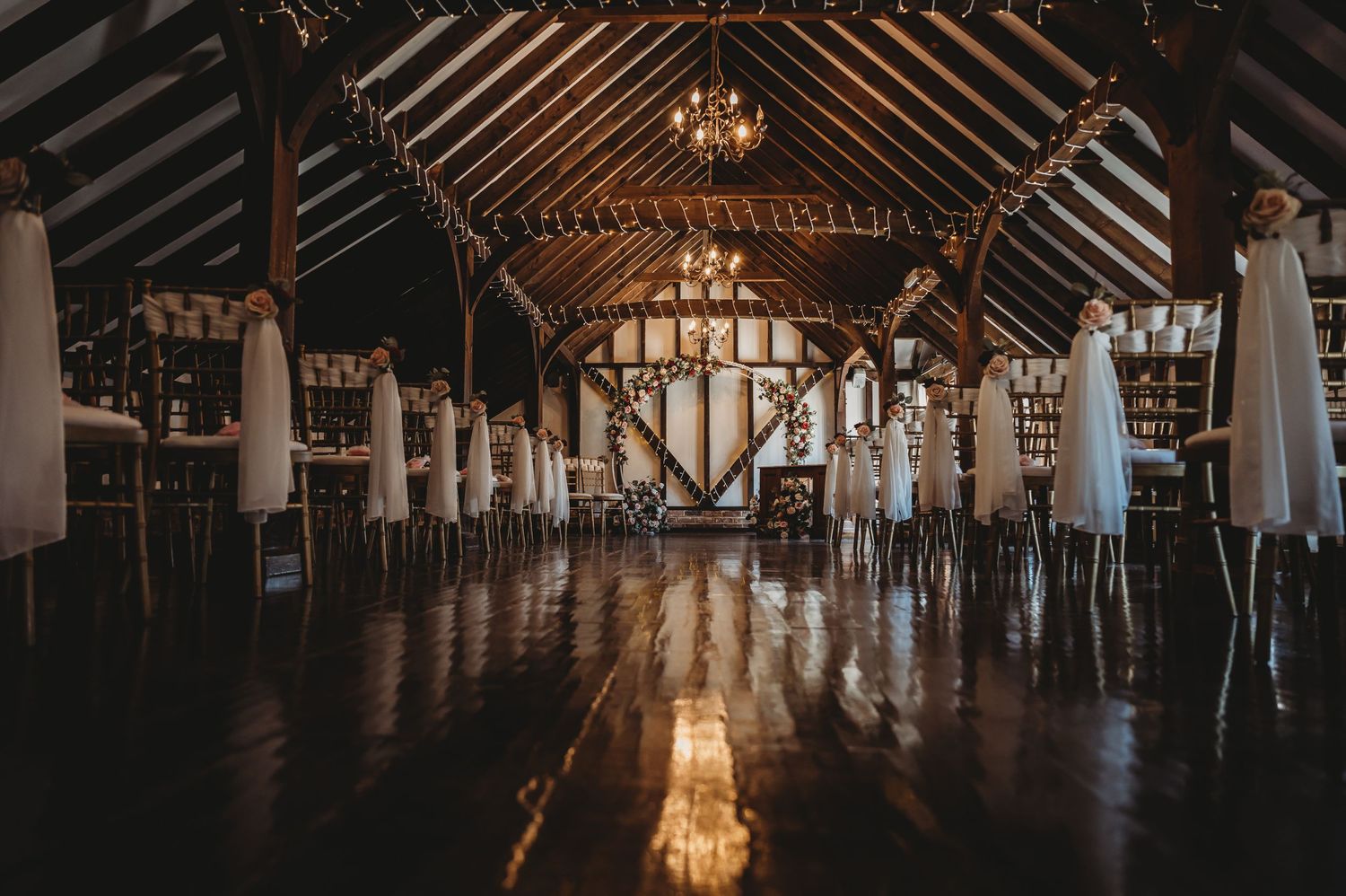Rustic barn venue interior with exposed wooden beams and white drapes set up for an elegant wedding reception.