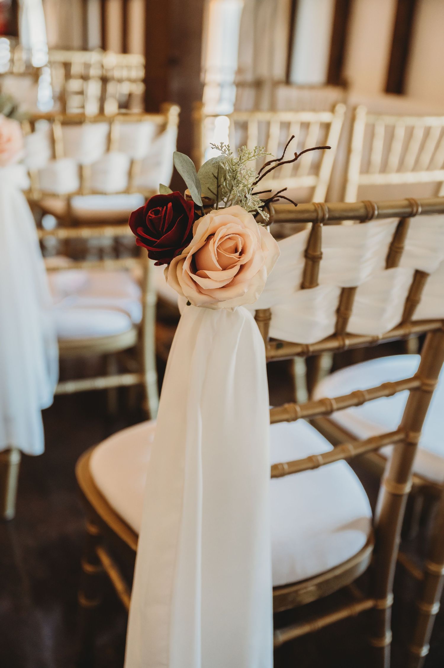 Elegant wedding chair decoration with burgundy and blush roses on white fabric draped over a gold chiavari chair.