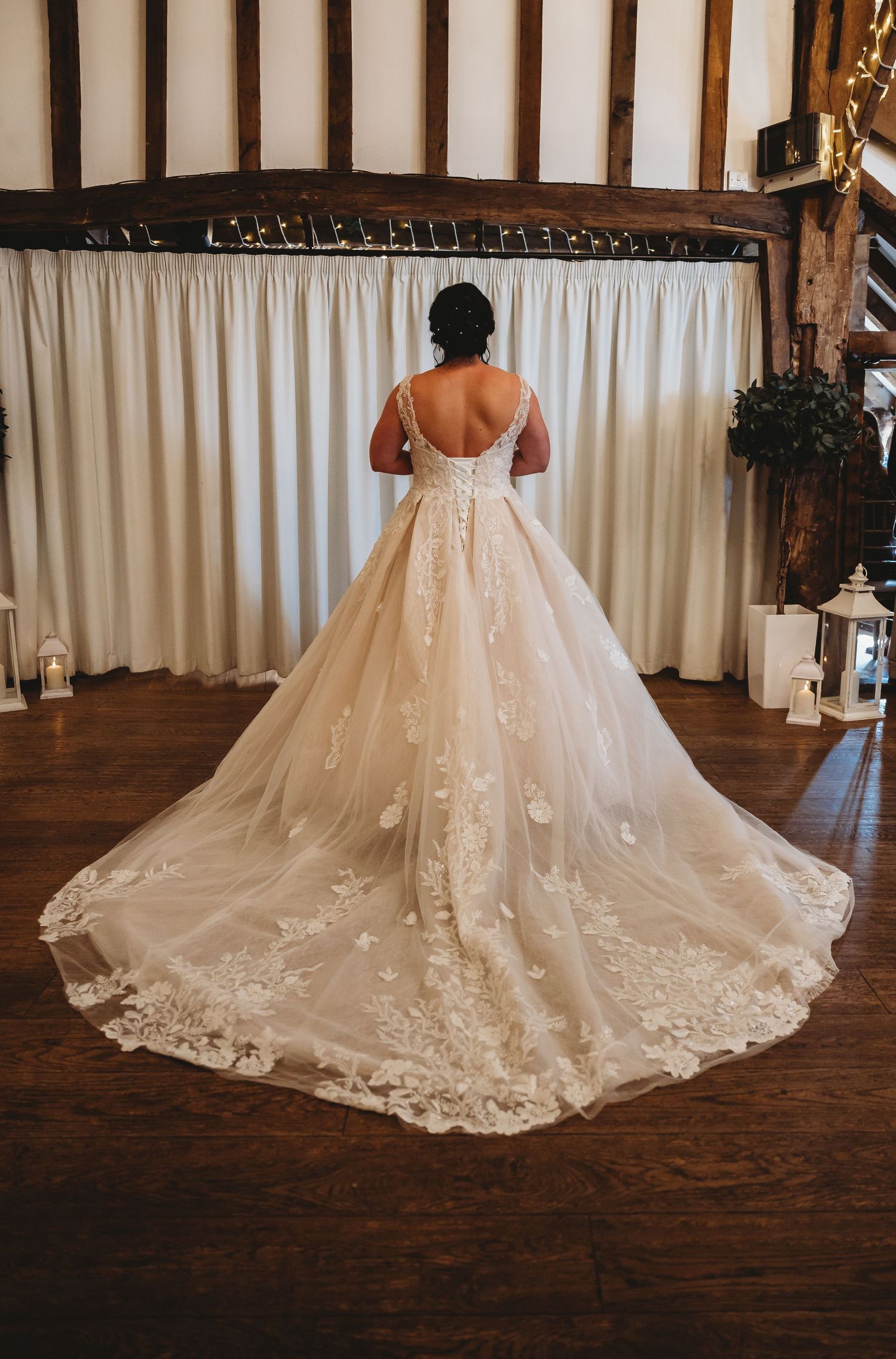 Back view of a bride in a stunning white ballgown wedding dress with lace details and long cathedral train on hardwood floor.
