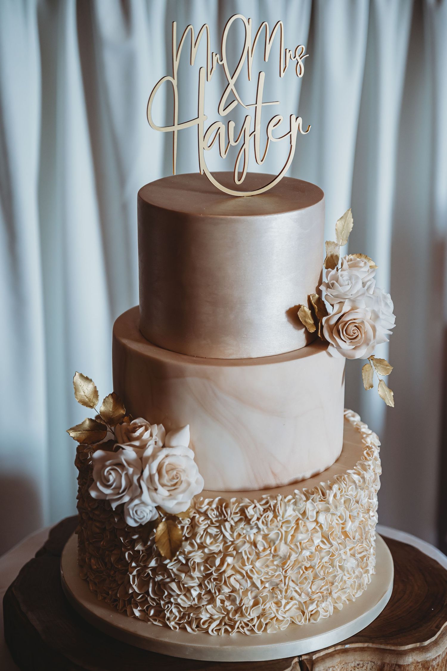 Elegant three-tier wedding cake with champagne ombré frosting, gold accents, and white roses topped with a Mr and Mrs topper.