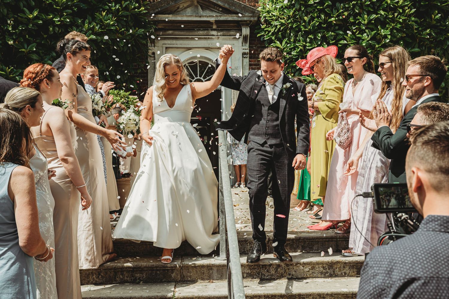 Newlyweds celebrate while exiting stone church steps surrounded by guests throwing flower petals.