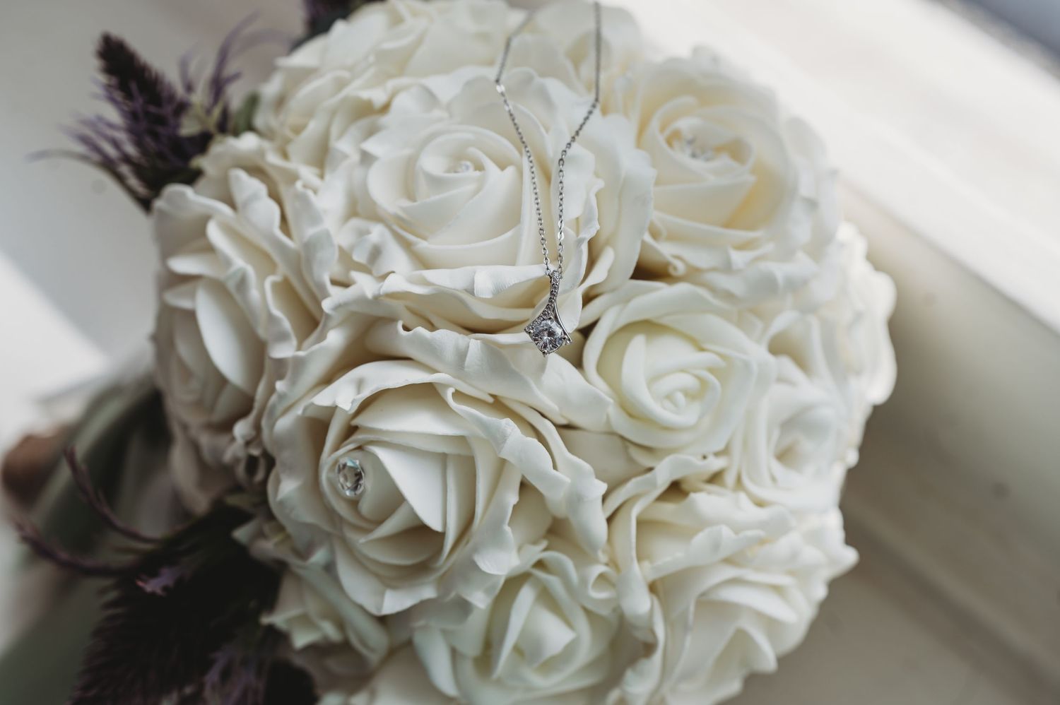 A delicate bouquet of white roses arranged in a spherical shape with soft feather accents.