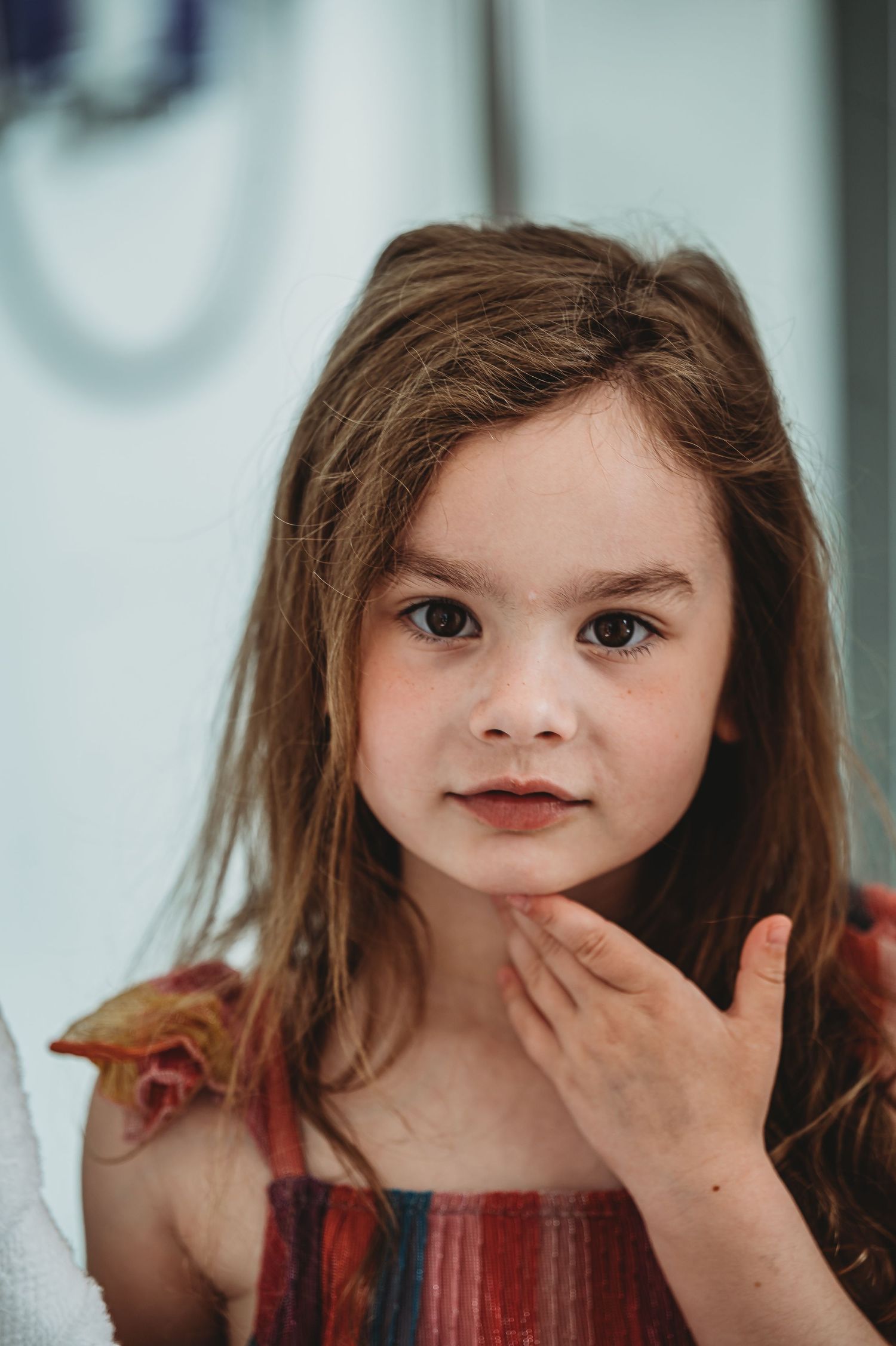 A young child with long brown hair and expressive eyes poses for a portrait while wearing a striped top.
