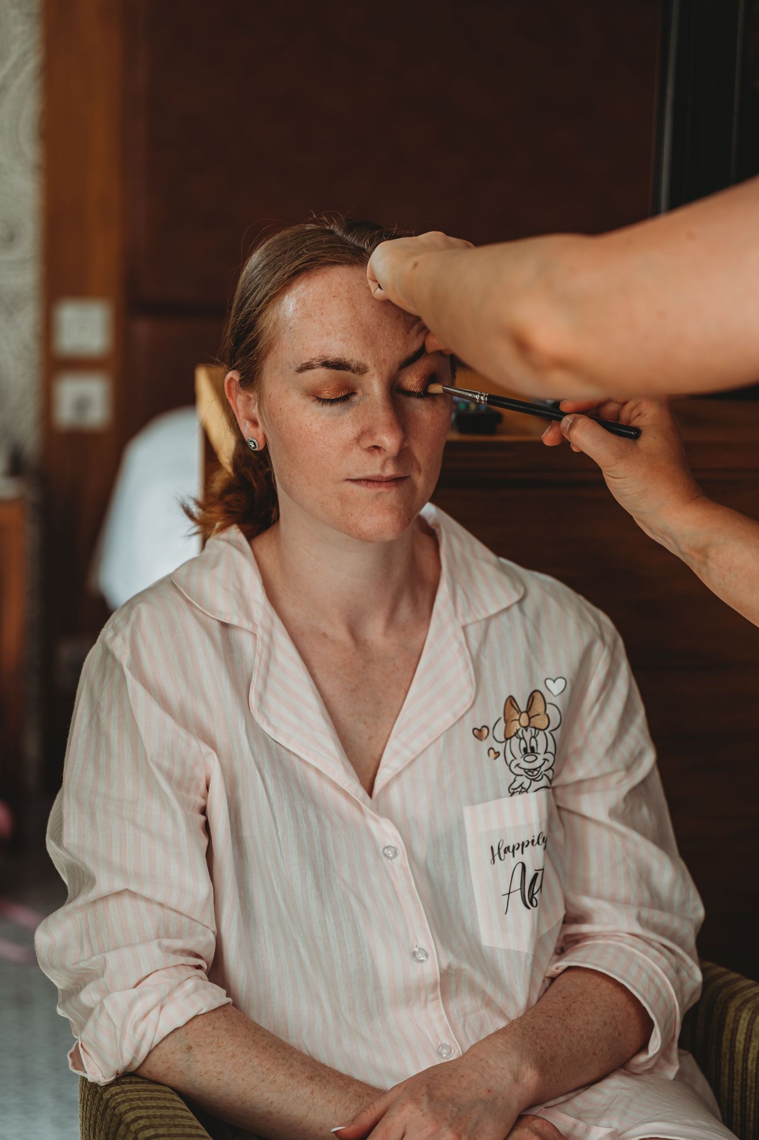 A person in a white embroidered robe receives professional makeup application during a beauty session.