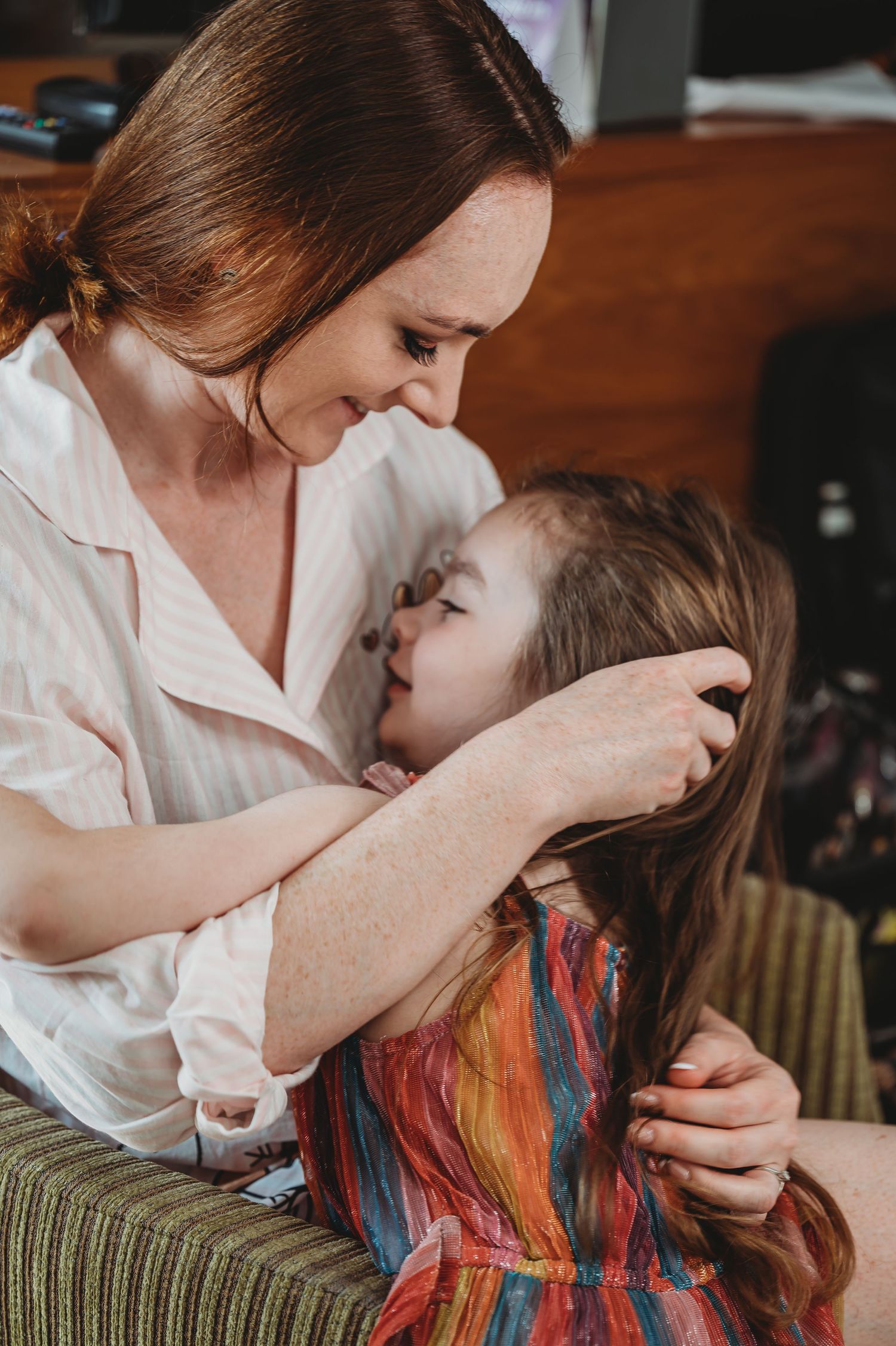 A tender moment shared between parent and child as they embrace on a green couch in a warm indoor setting.