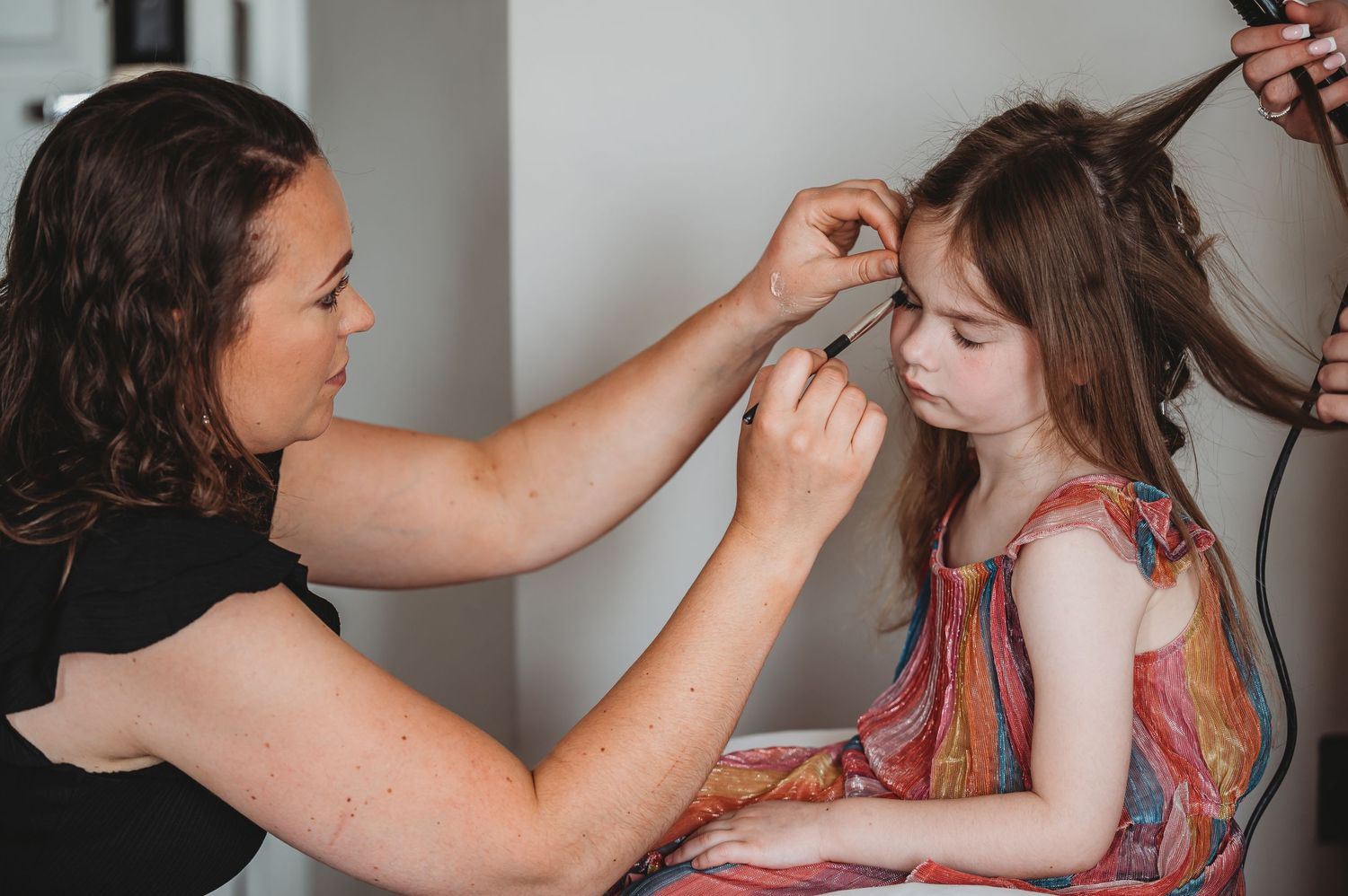 A young child sits patiently while getting hair and makeup done for a special occasion.