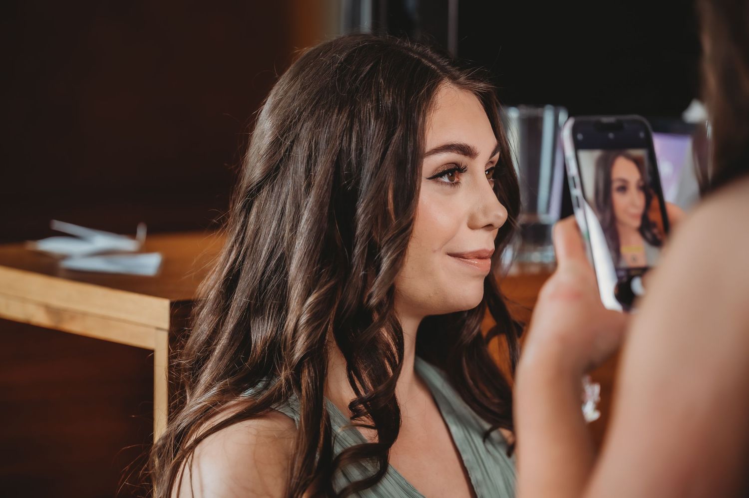 A stylist creates curls in dark hair while an image is captured from behind in a salon setting.