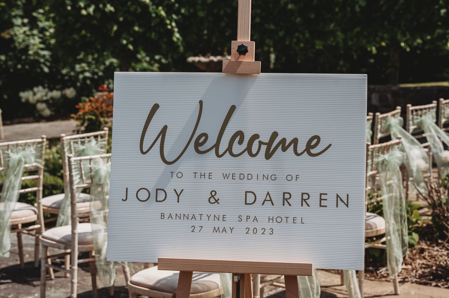 White welcome sign for a wedding at Barnsley Spa Hotel displays elegant lettering and event details on an easel outdoors.