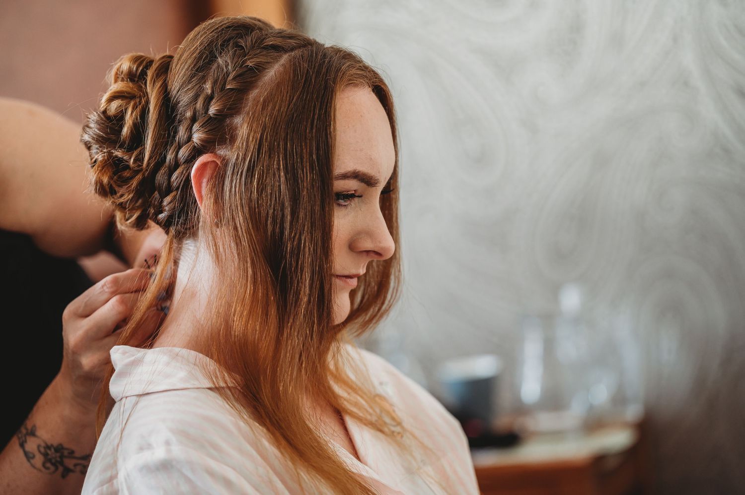 Hairstylist creates an intricate updo on long brown hair in a warm-toned salon setting.