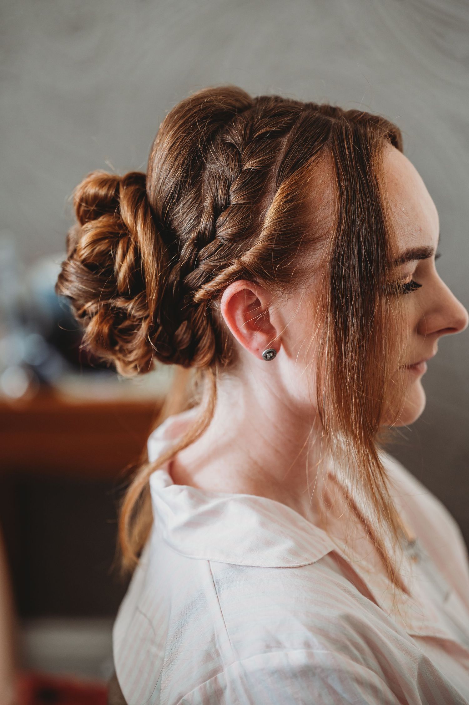 Side profile view of an elegant updo hairstyle with braided details and loose strands, styled for a special occasion.