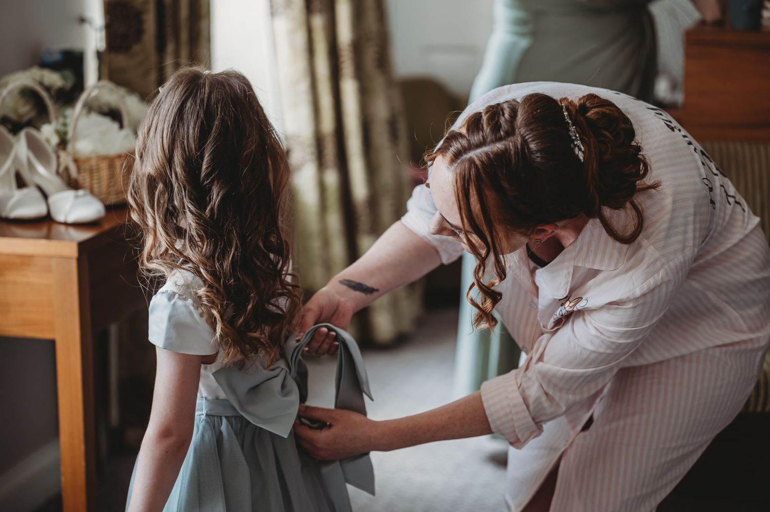 Woman in white adjusts a grey dress on a young girl in a tender moment at home.