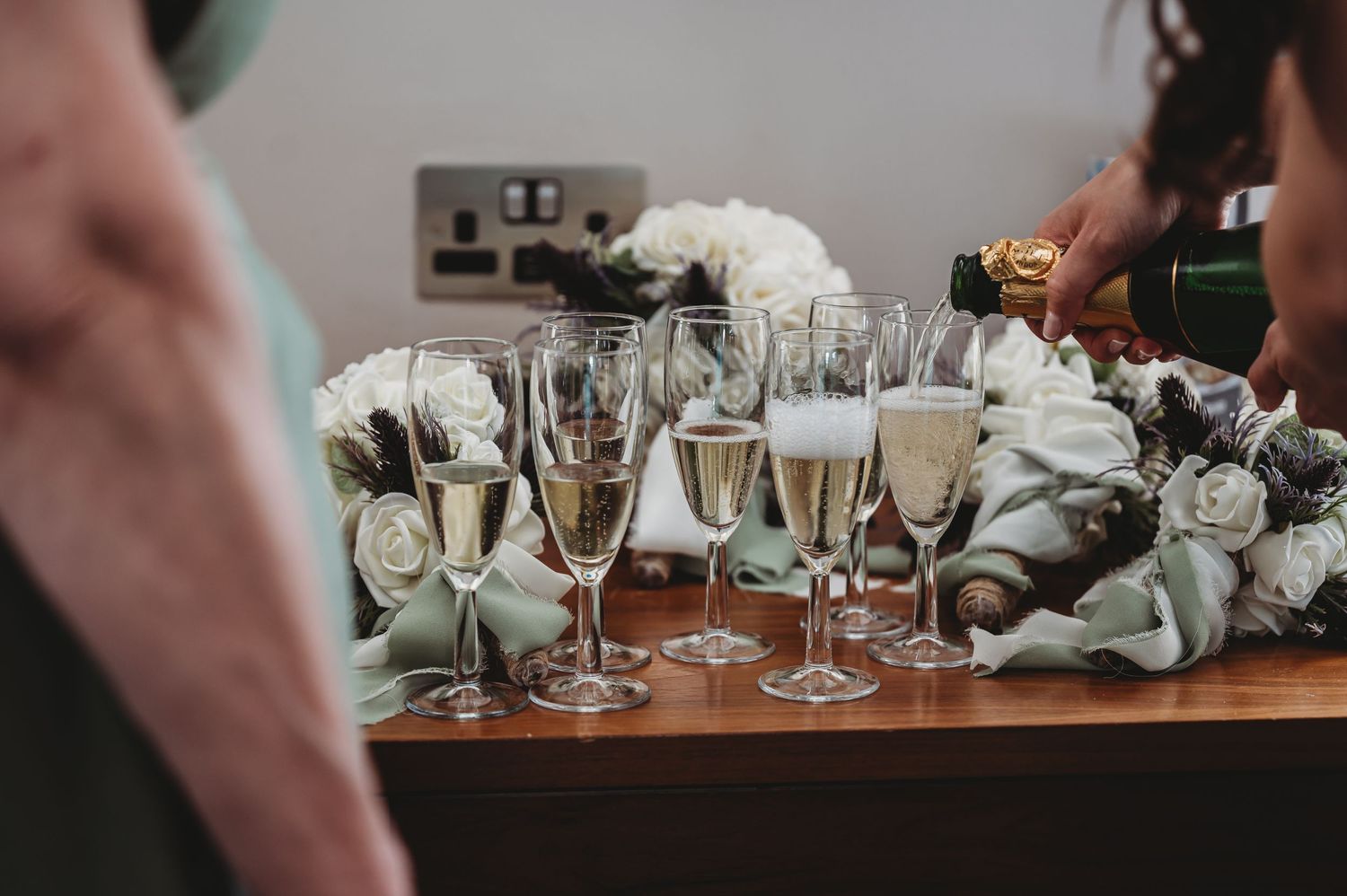 Several champagne glasses on a wooden table with white roses and decorative table settings.