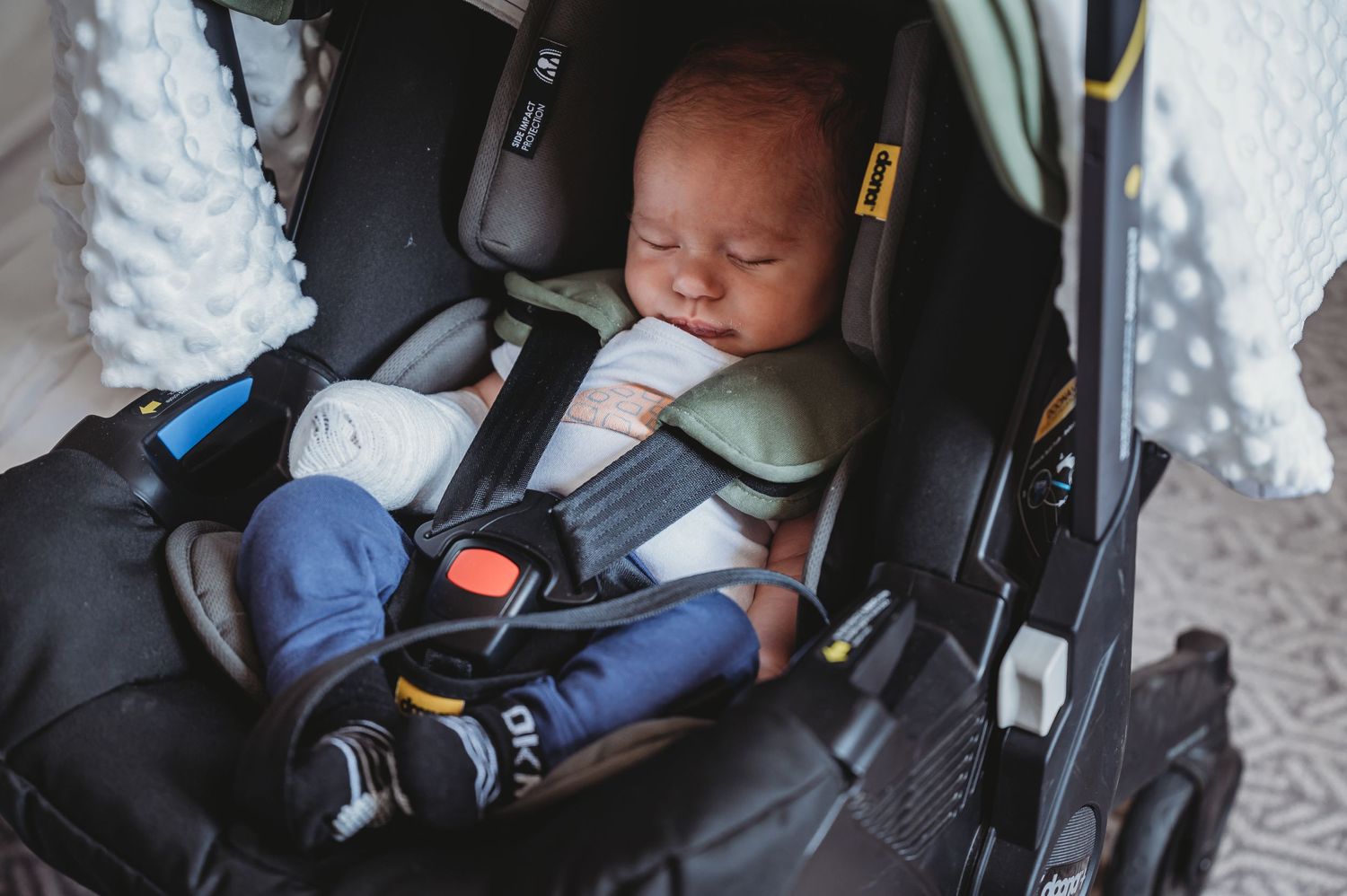 A peaceful baby sleeping in a black car seat secured with safety straps and harness.