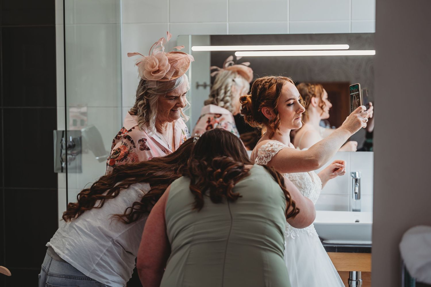 A group huddles together in a bathroom getting ready during pre-wedding preparations with excitement and laughter.