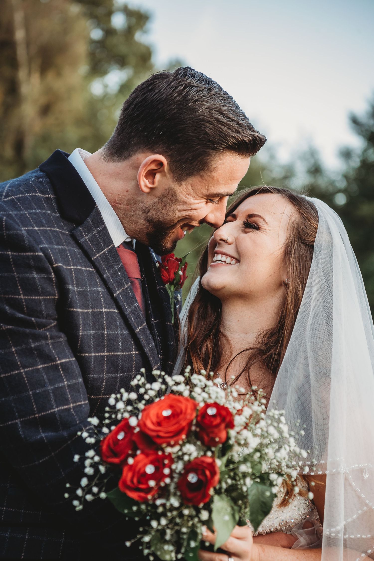 A couple shares an intimate moment on their wedding day with a bouquet of red roses and baby's breath.
