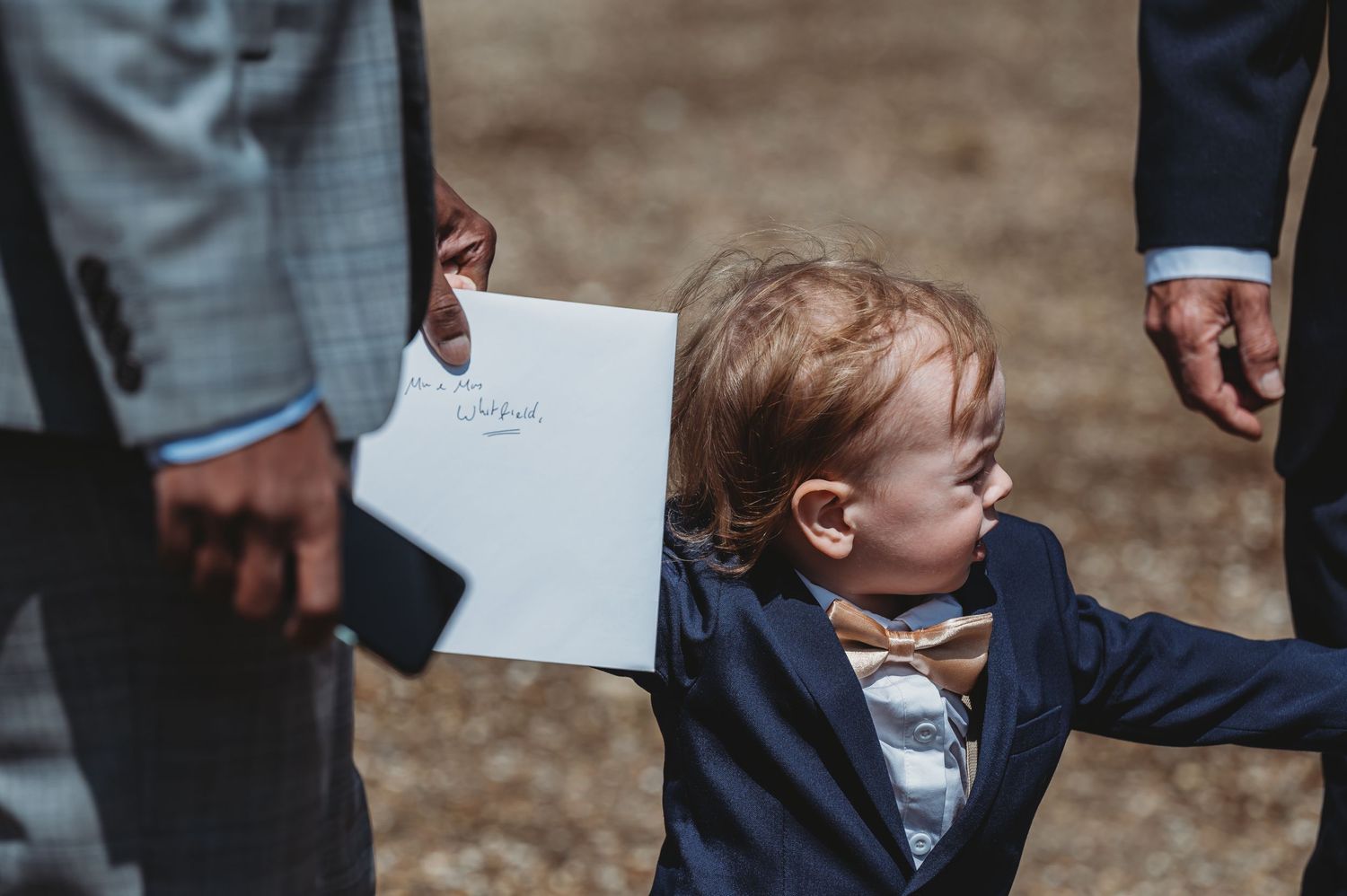 Young child in a navy blazer reaches up while holding a paper at an outdoor event.