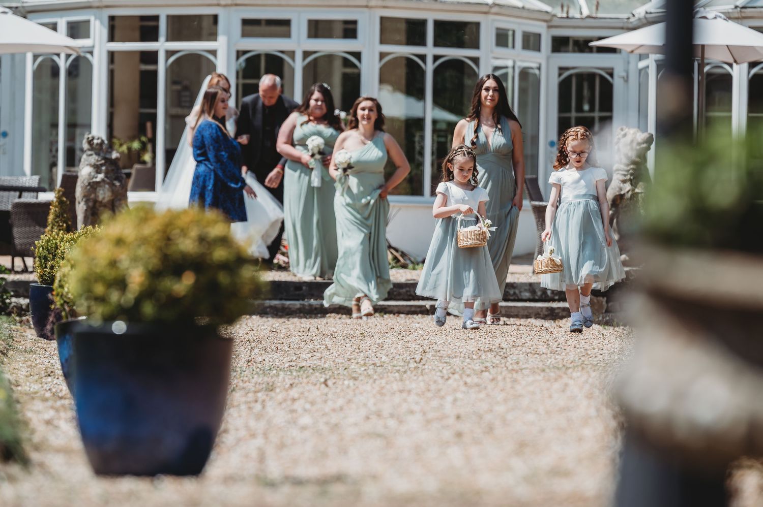 Wedding party in light blue bridesmaid dresses walking together outside an elegant white gazebo building.