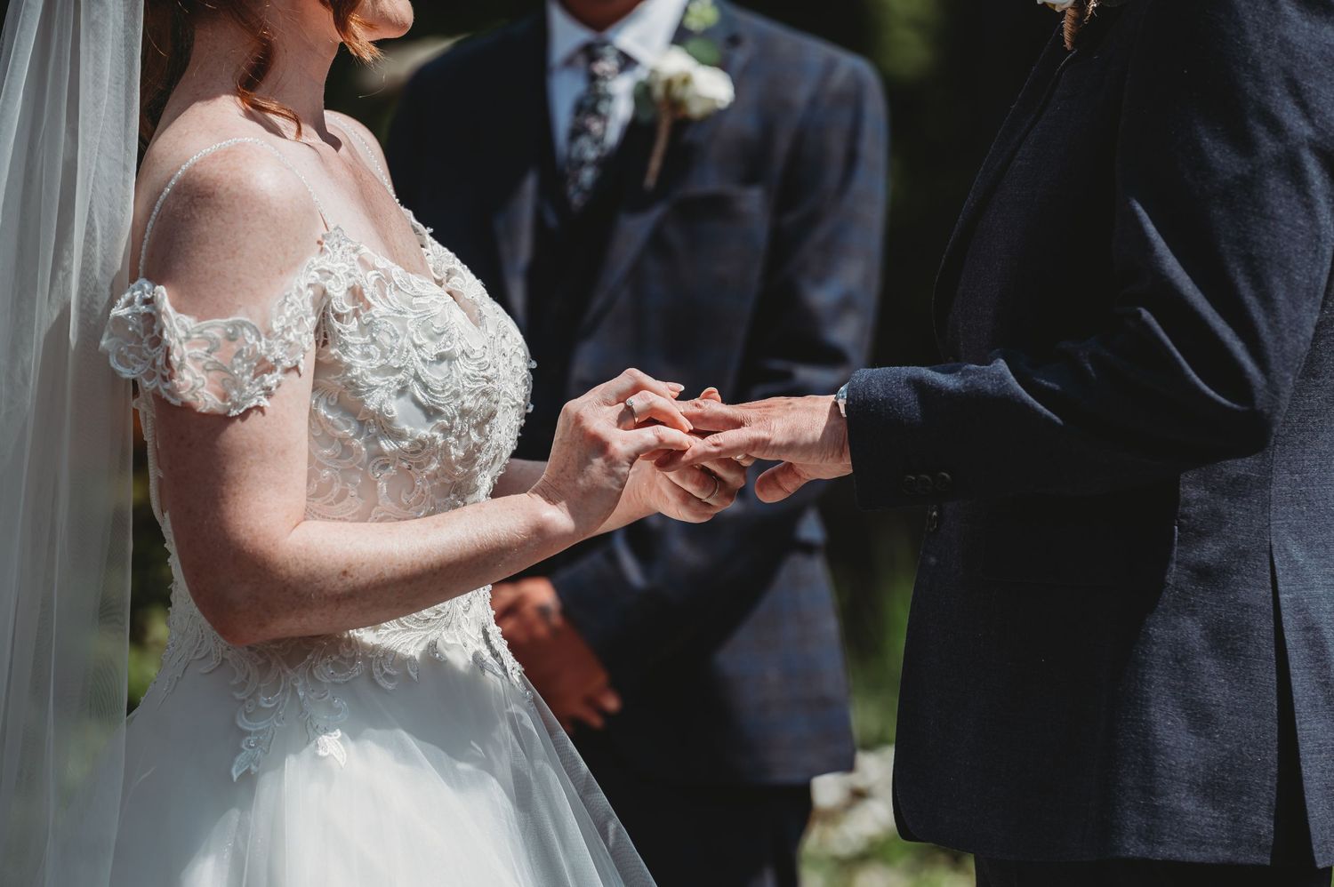 Close-up shot of wedding ceremony ring exchange with delicate lace details on bridal gown visible.