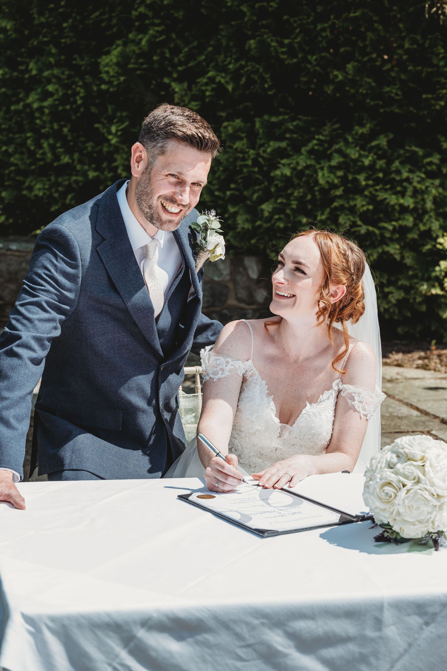 A happy couple shares a joyful moment while signing their marriage certificate at an outdoor wedding ceremony.
