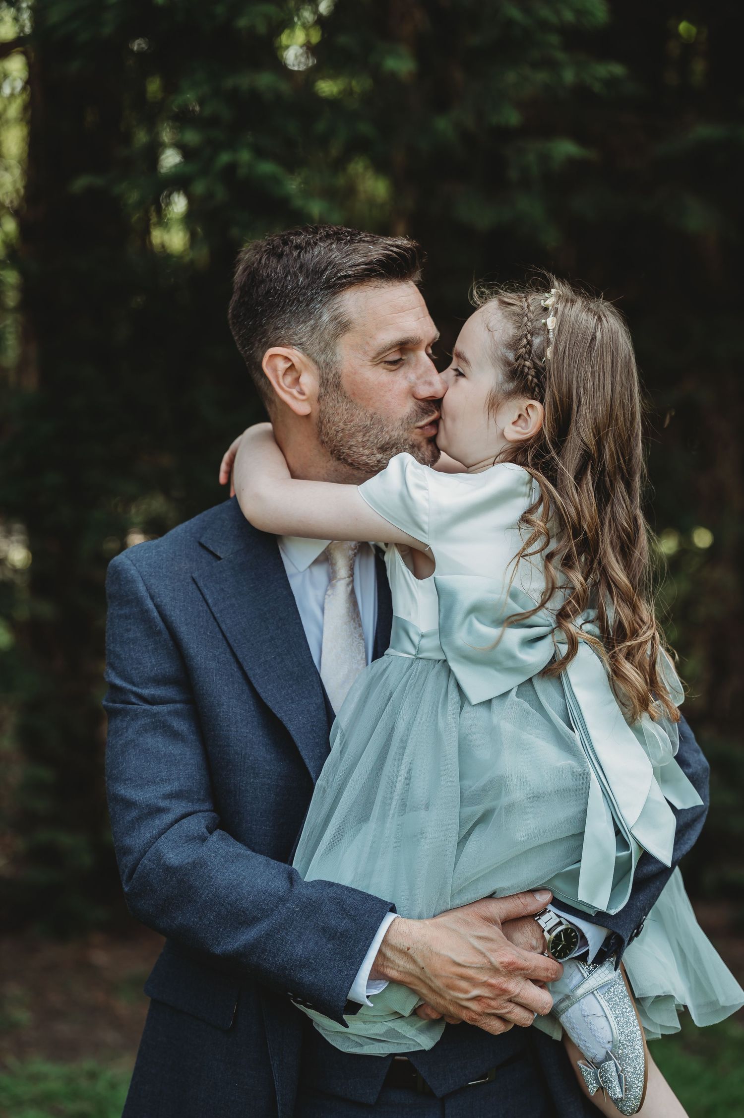 An intimate father-daughter moment captured during a wedding celebration in a wooded setting.