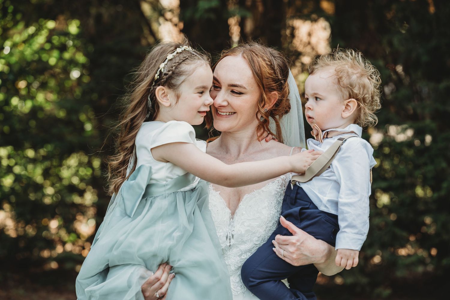 A joyful family moment captured outdoors in a wooded setting with natural sunlight filtering through the trees.